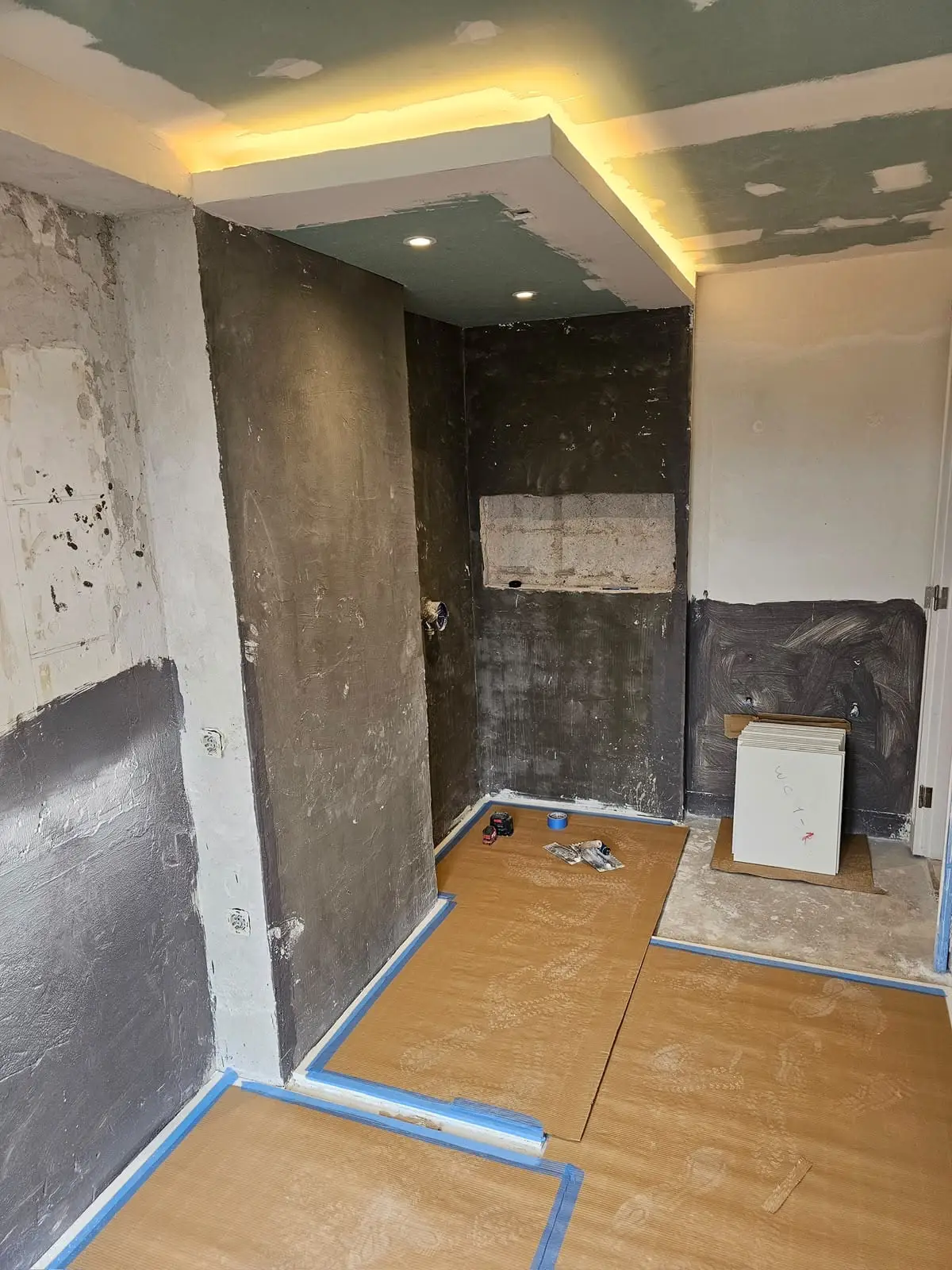 Bathroom stripped back to bare walls with waterproofing applied and the floor covered in protection board