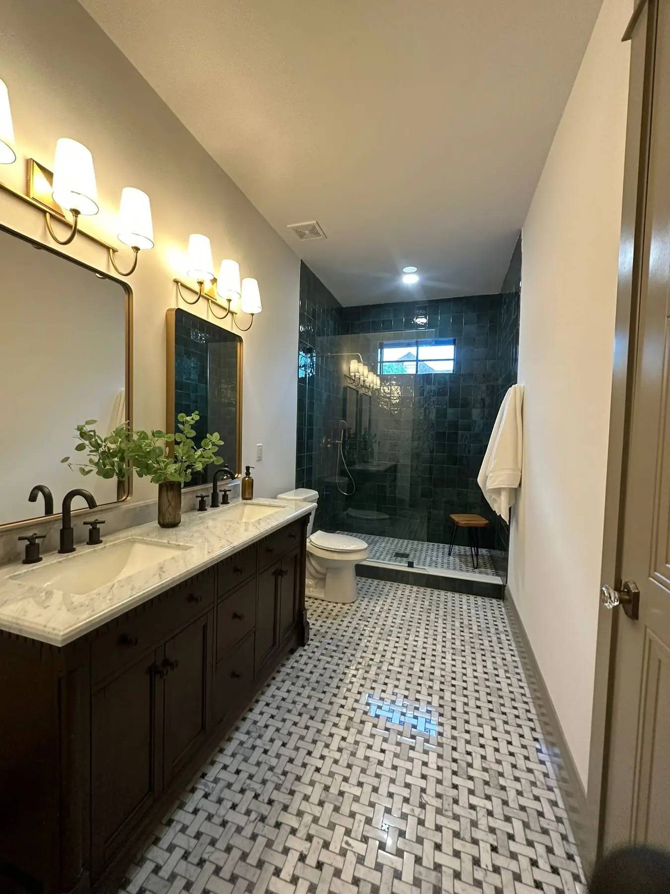 Bathroom with a walk-in shower tiled in deep green zellige, a dark double vanity with a marble top and a basketweave marble floor, by General Tile Company