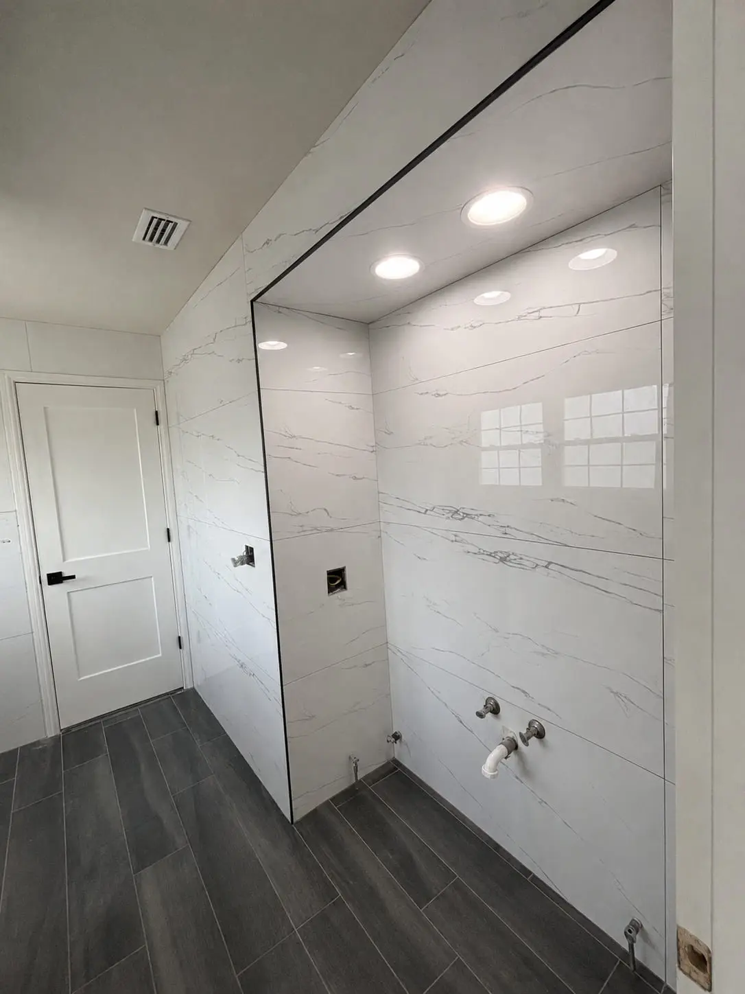Walk-in shower lined in marble-look porcelain with a frameless glass panel, by General Tile Company