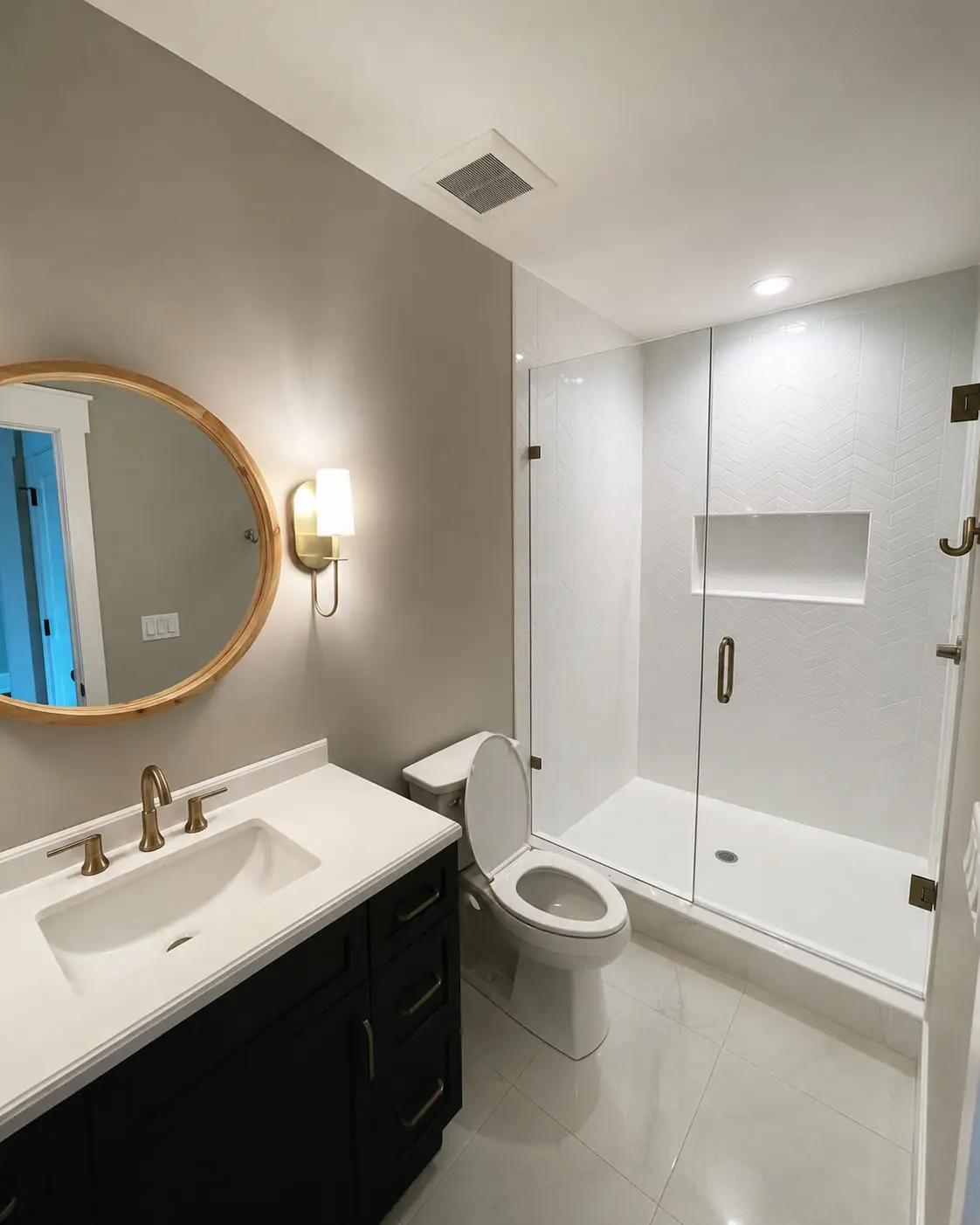 Completed bathroom remodel with a dark vanity, round mirror and a frameless glass shower, by General Tile Company