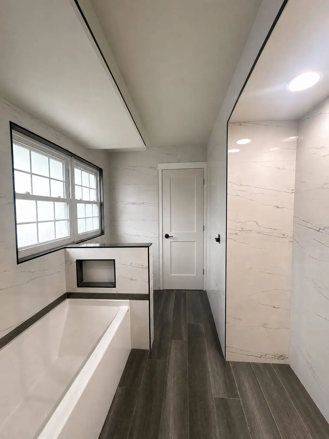 Bathroom with a built-in tub and walk-in shower finished in the same marble-look tile, lit by a window at the far end