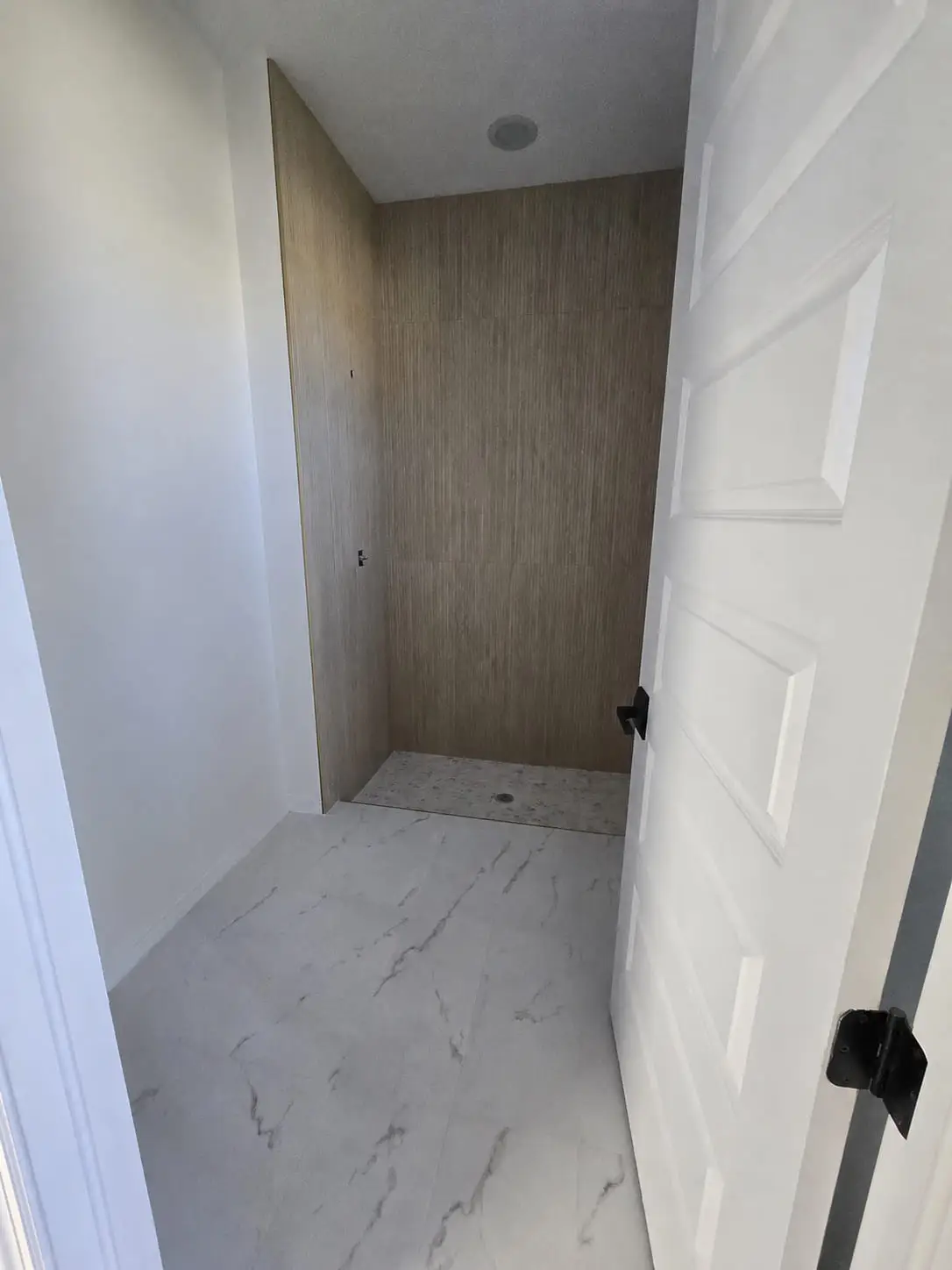 Shower finished in wood-look porcelain running floor to ceiling, with a marble-look floor at the threshold