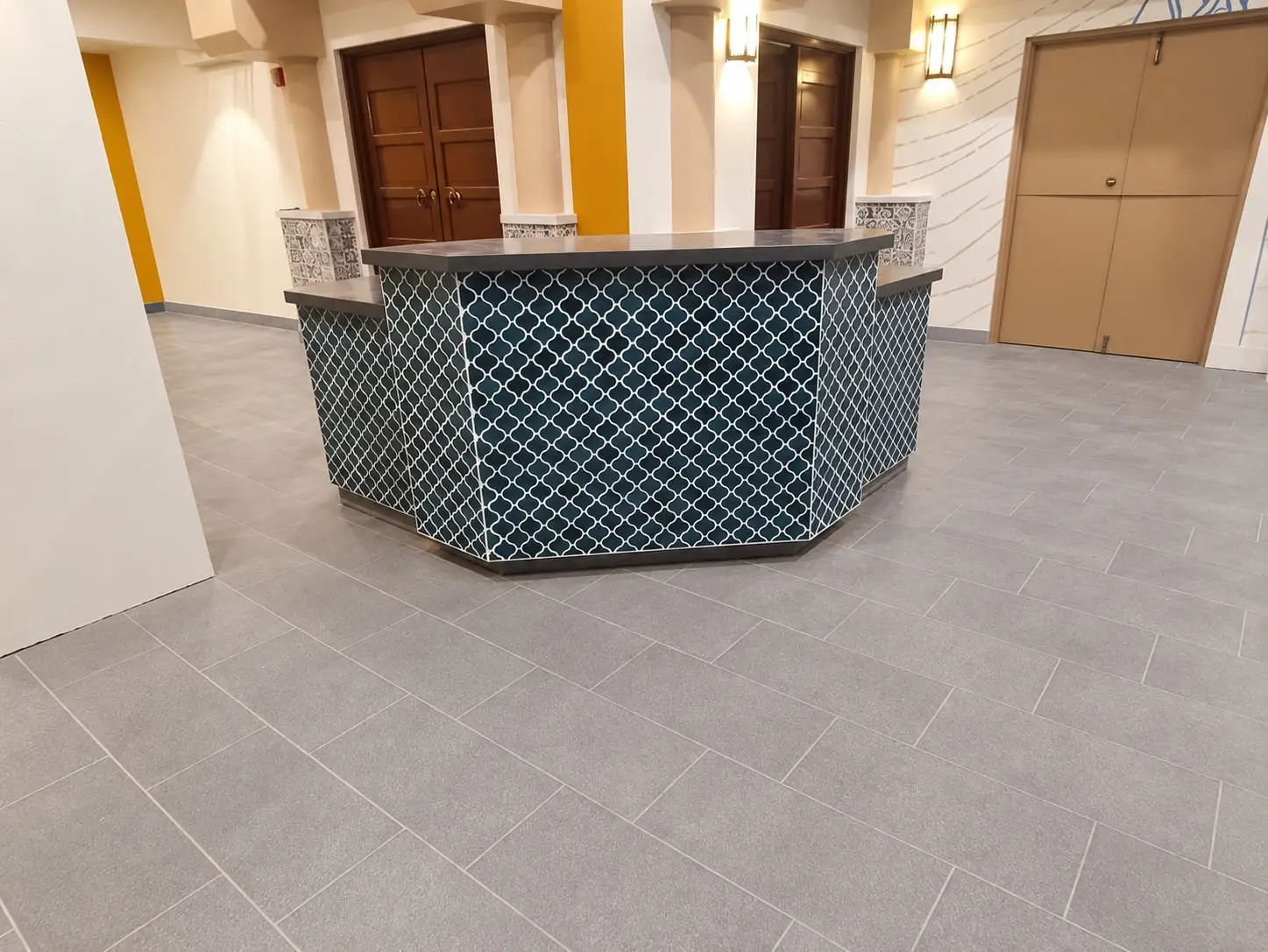 Reception desk clad in deep blue arabesque tile with a stone top, on a large-format grey floor, by General Tile Company