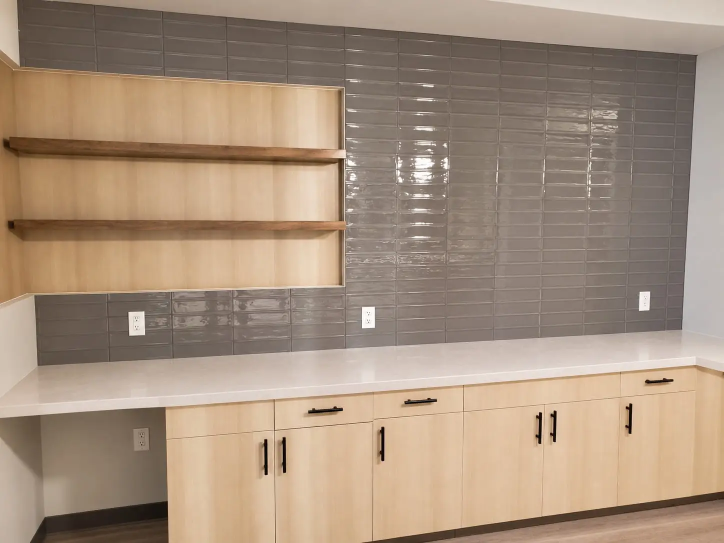 Break-room wall in glossy grey subway tile with floating timber shelves above light wood cabinets