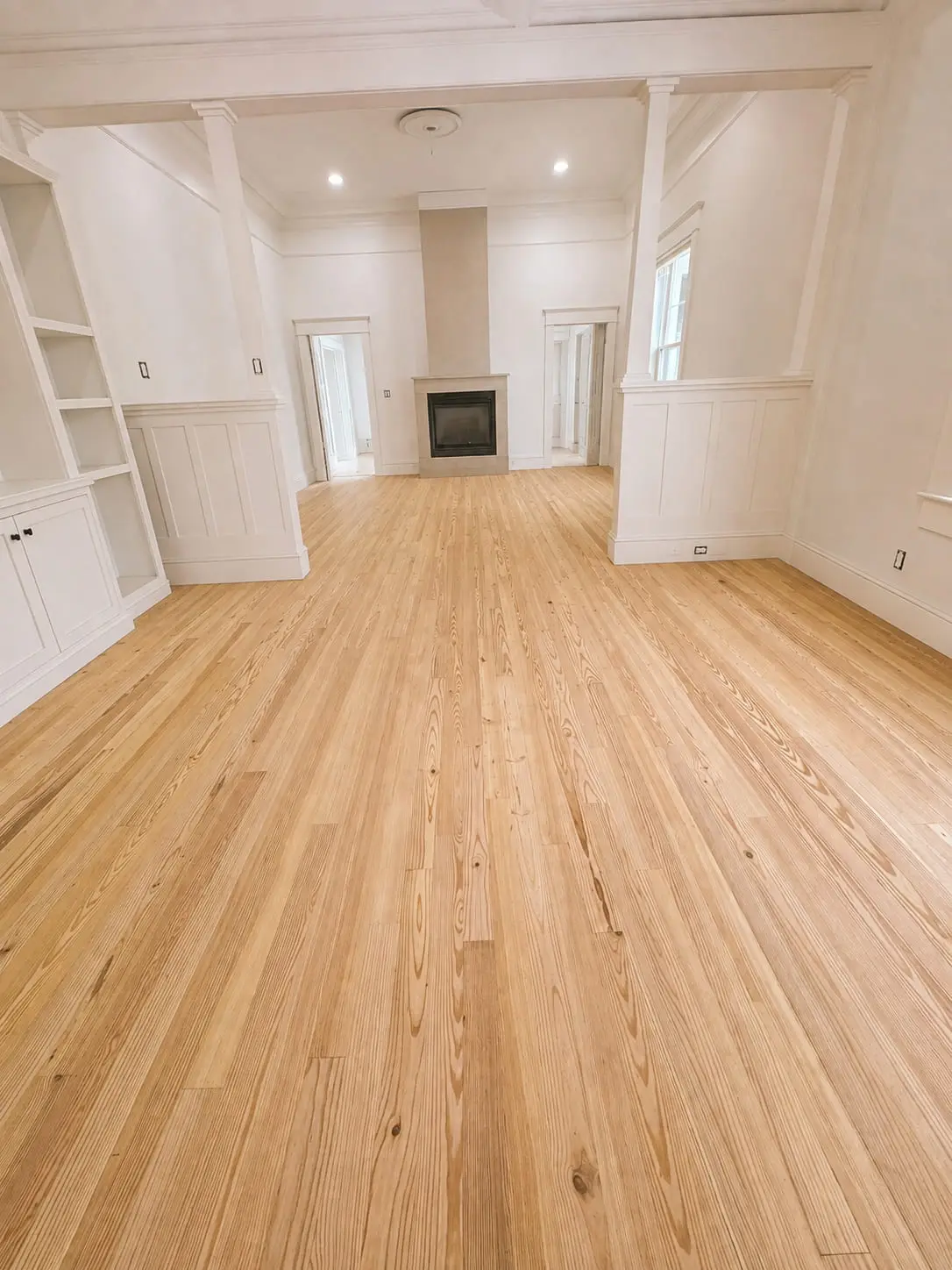 Wide-plank wood floor running the length of a living room and straight past a built-in fireplace, installed by General Tile Company