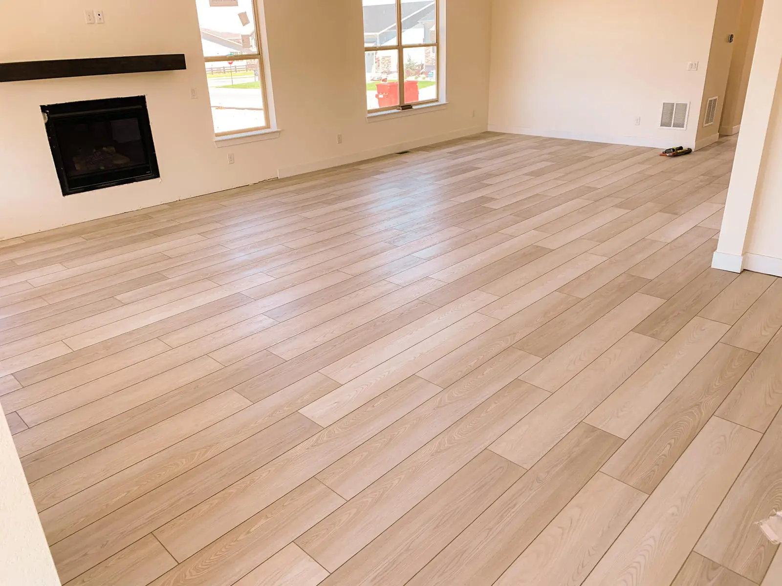 Wide light plank floor laid in a single direction across an open living room, carried straight through the doorway