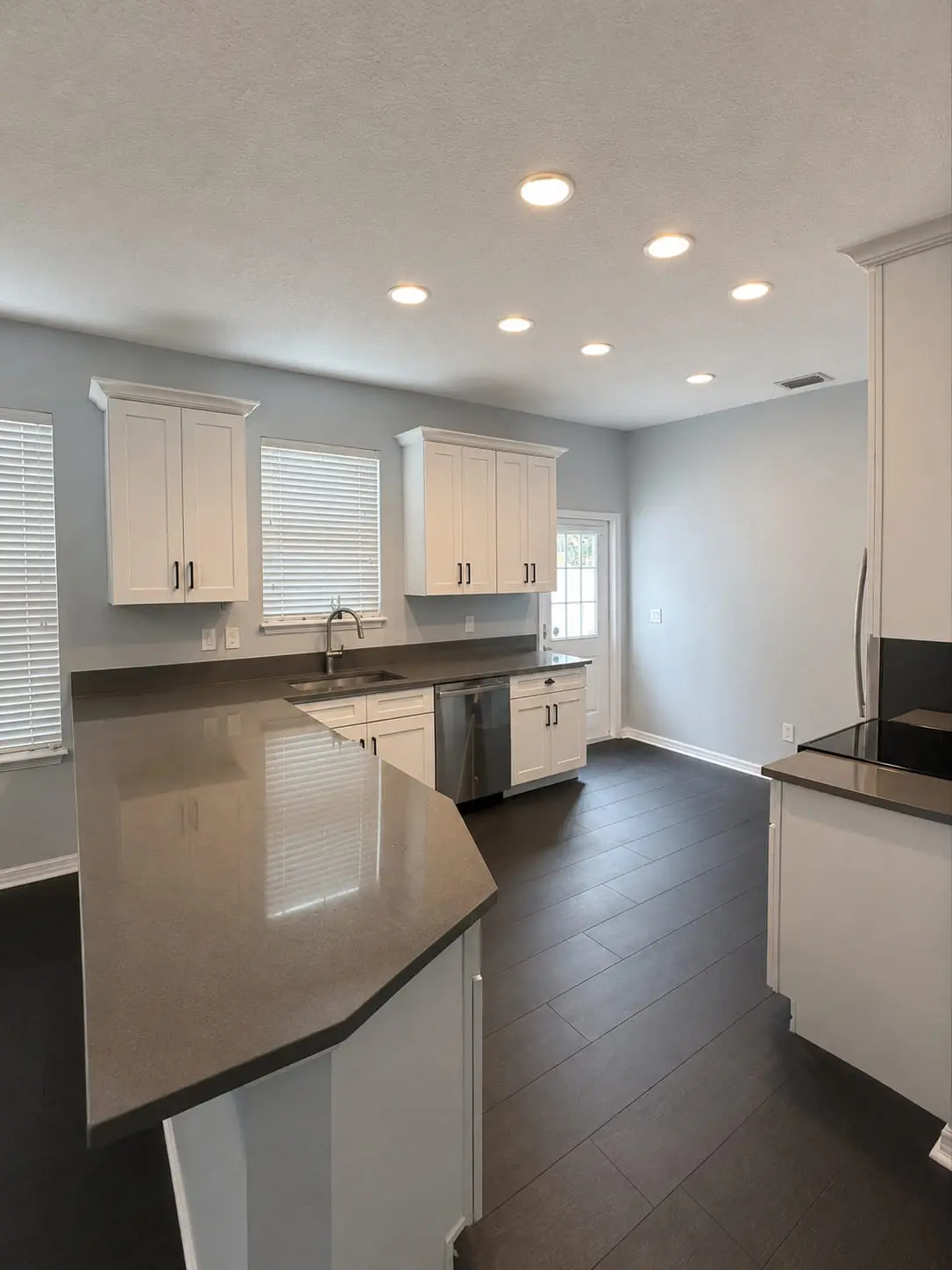Angled kitchen peninsula with a dark stone counter and white cabinetry over a dark plank floor