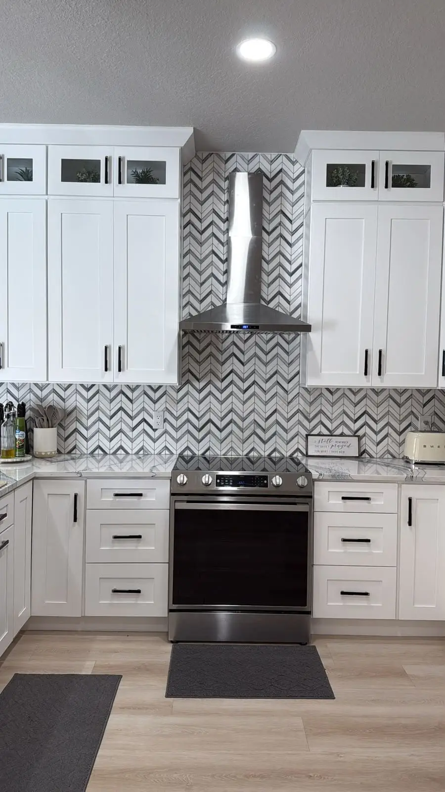 White shaker kitchen with a chevron marble mosaic backsplash running between the wall cabinets and behind the range hood