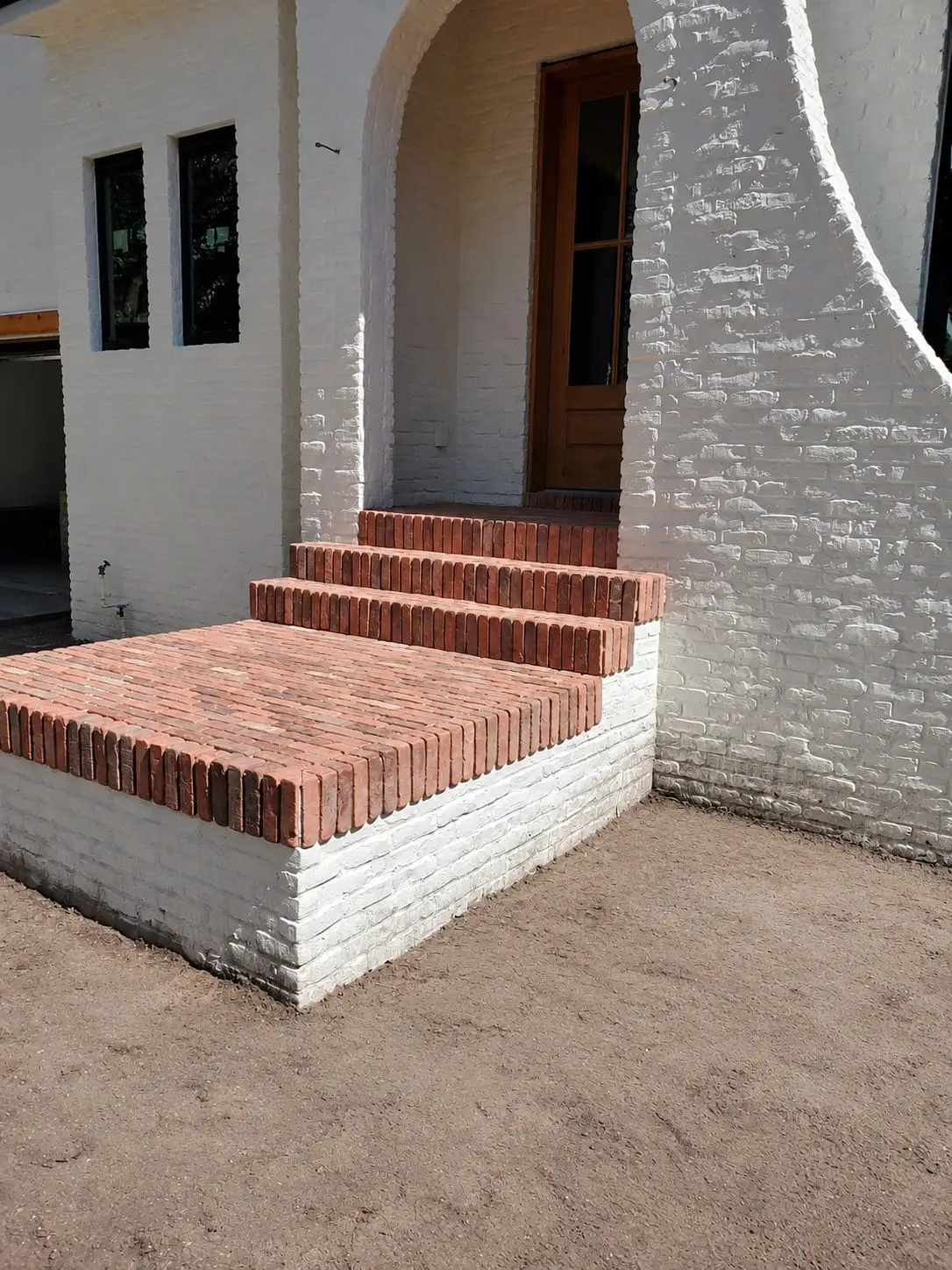 Newly built brick entrance steps against a white house, with the ground around them still to be finished