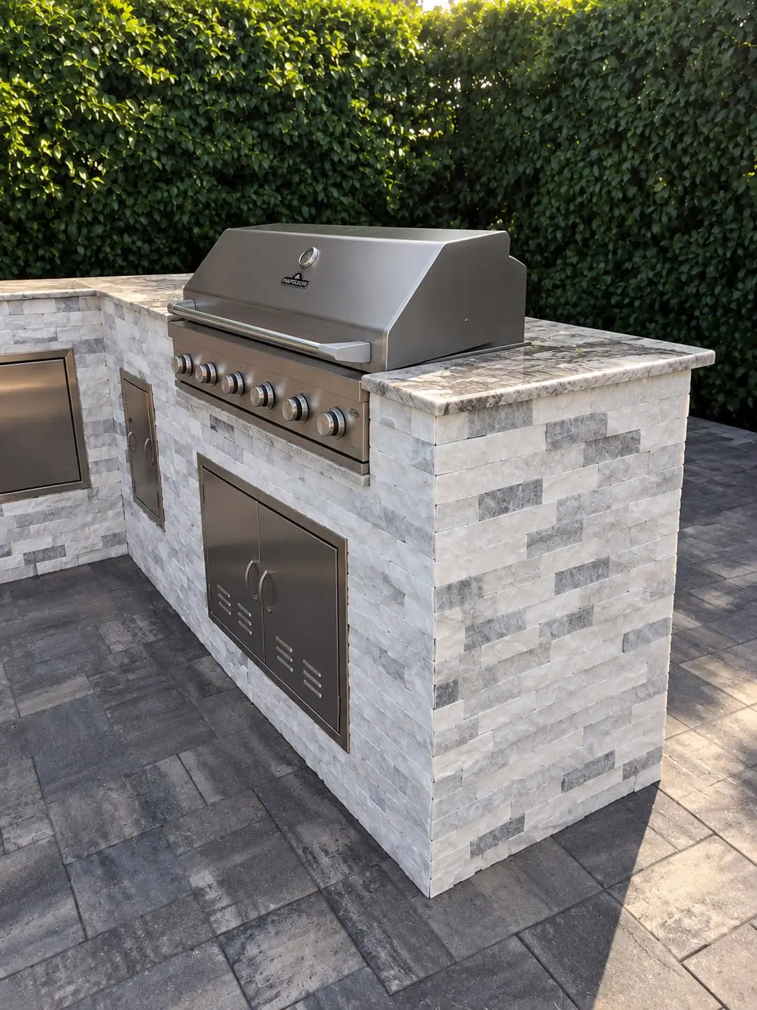 Outdoor kitchen with a built-in stainless grill, clad in white stacked stone ledger on a paver deck, by General Tile Company