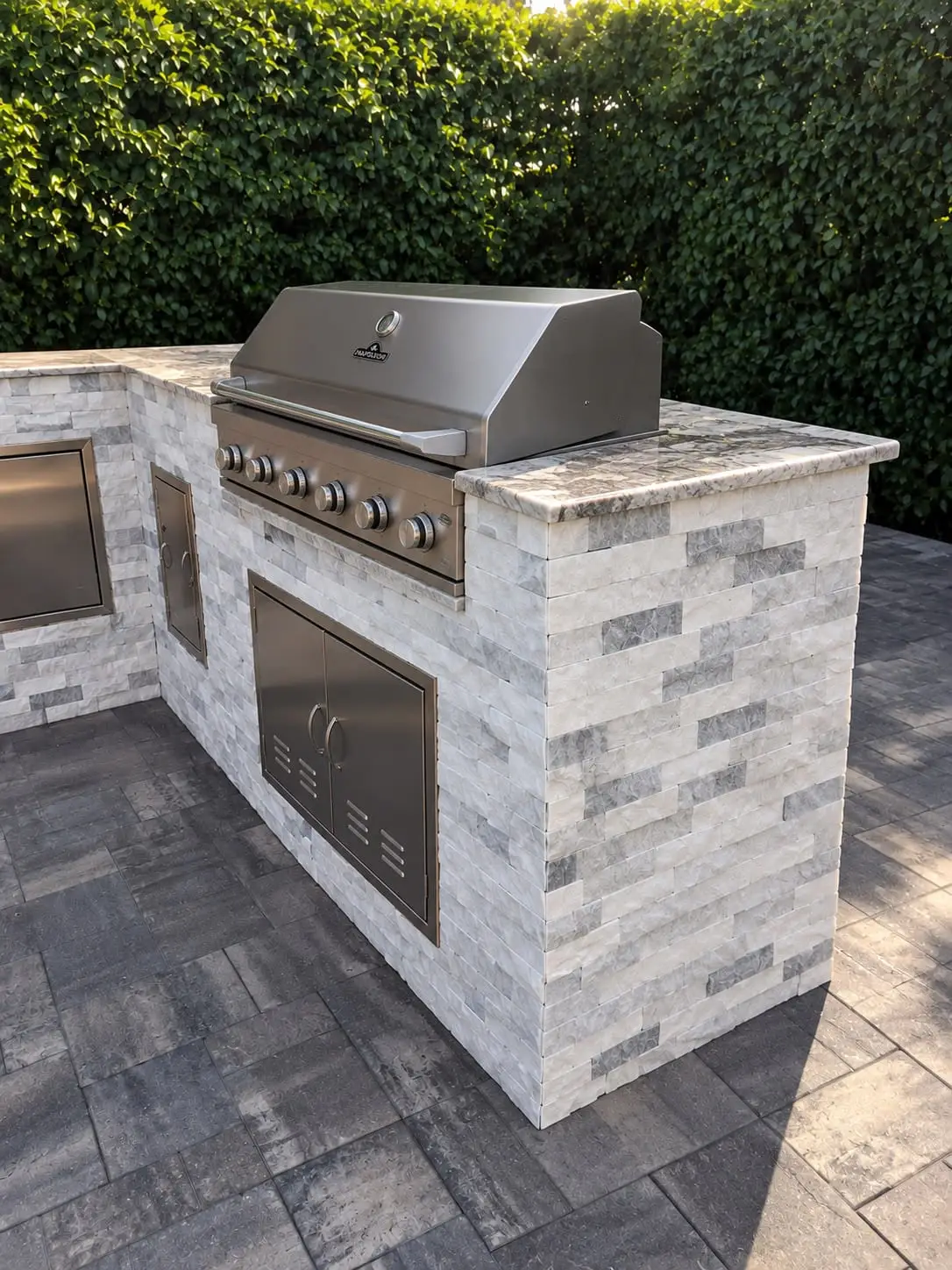 Outdoor kitchen with a built-in stainless grill, clad in white stacked stone ledger on a paver deck, by General Tile Company
