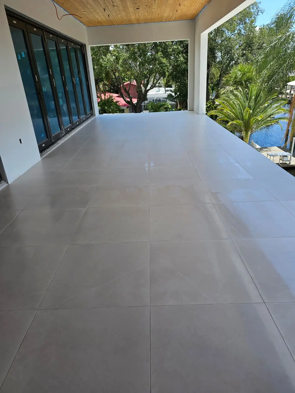 Covered lanai floored in large-format grey porcelain, running out to a waterfront view between folding glass doors