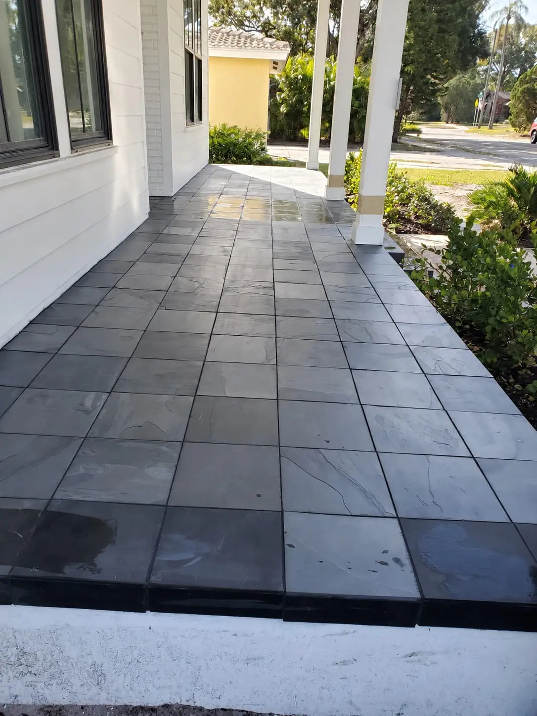 Walkway beside a house laid in dark slate-look porcelain, running between the wall and a row of columns