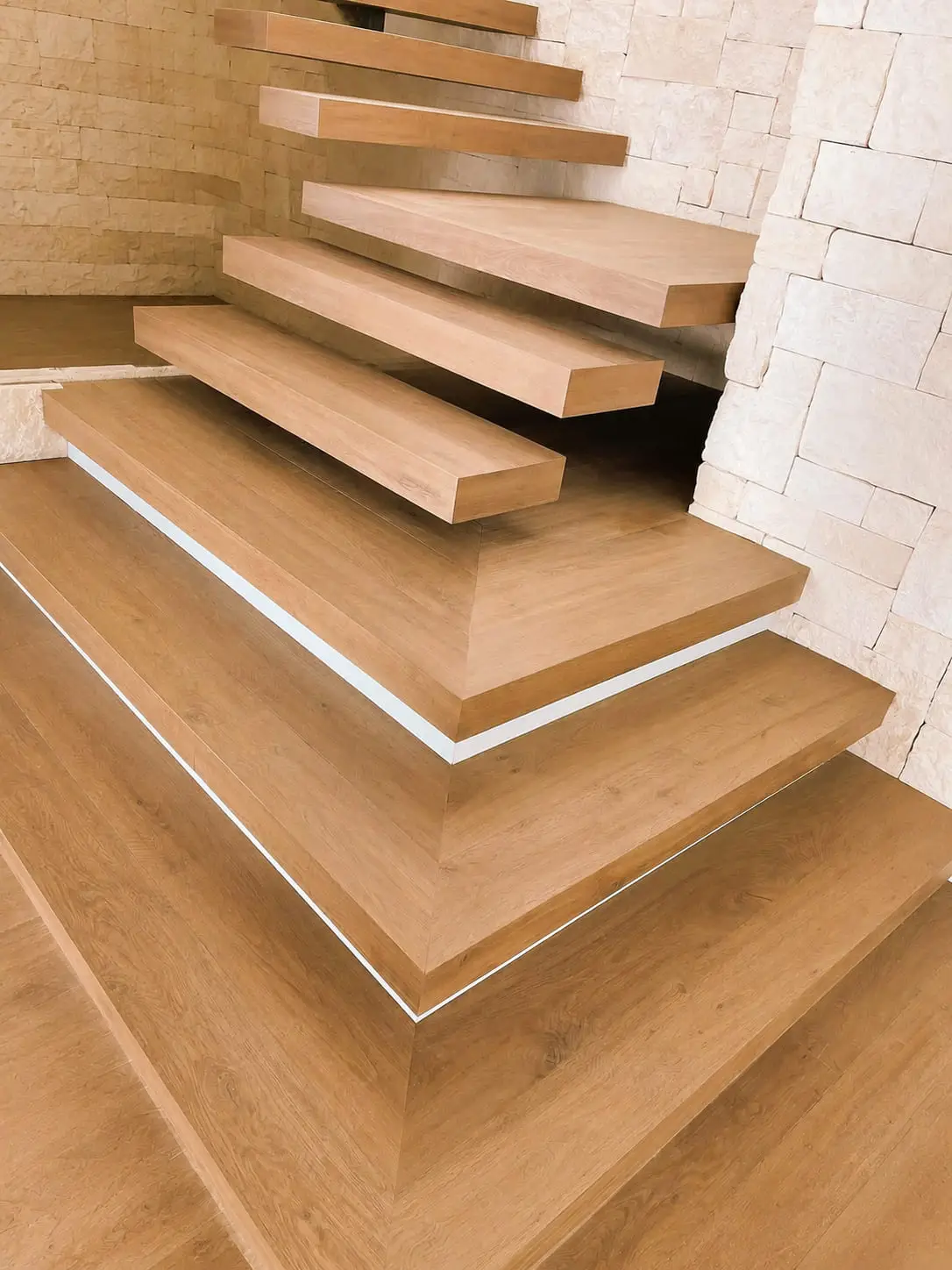 Floating oak stair treads cantilevered from a rustic stone wall, installed by General Tile Company in Tampa Bay
